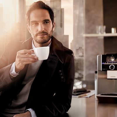 Culture café Siemens : un homme boit du café dans une cuisine. Machine à café tout automatique Siemens EQ.9 posée sur la table