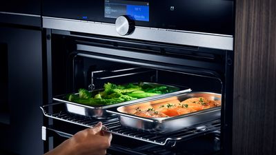 Siemens : une main enfourne des plaques avec des légumes et du poisson cuits à la vapeur