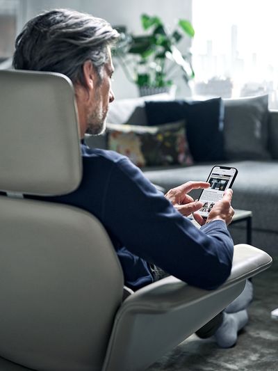 Link öffnet die Übersichtsseite für Siemens Home Connect; ein Mann im Sessel bedient seinen Siemens Geschirrspüler per Smartphone