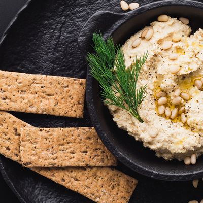 Multiple cheesy vegan crackers with a bowl of hummus