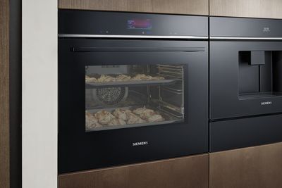 Four moderne Siemens avec une porte en verre révélant les produits de boulangerie à l'intérieur, doté d'un affichage numérique et intégré dans une cuisine au design épuré.