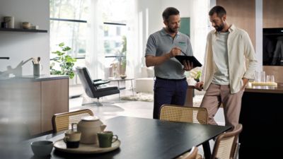 Un technicien de service Siemens explique quelque chose à un client sur une tablette dans une cuisine ouverte moderne