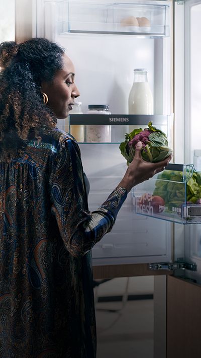 Eine Frau holt frisches Gemüse aus einer Kühl-Gefrier-Kombination von Siemens