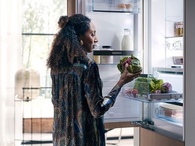 Eine Frau holt frisches Gemüse aus der hyperFresh-Schublade einer Kühl-Gefrier-Kombination von Siemens