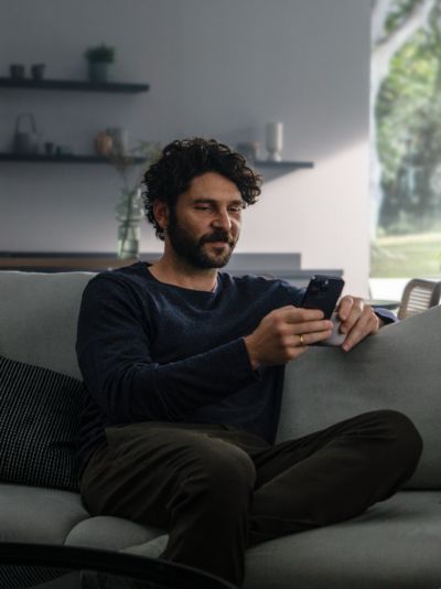 Eine Person sitzt auf einer grauen Couch und benutzt ein Smartphone.