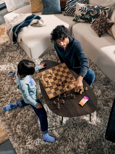 Ein erwachsener Mann spielt mit einem Kind Schach auf einem Couchtisch.