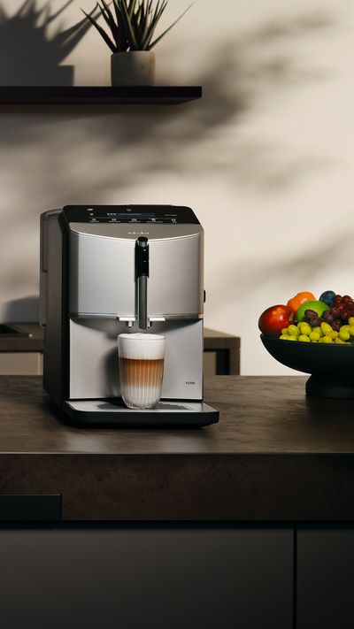 Küche mit dem EQ300 Kaffeevollautomaten auf einer Kücheninsel, ein Glas Latte Macchiato steht unter dem Auslauf. 