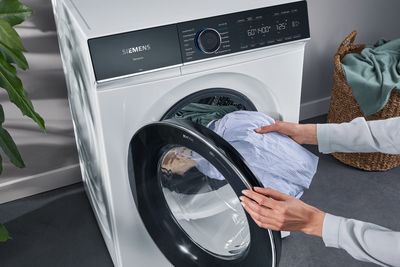 Eine Person legt Wäsche in eine moderne Siemens iQ700 Waschmaschine.