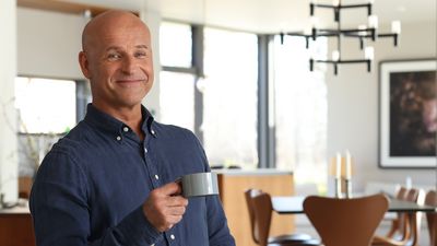 Richard Juhlin holder en kop kaffe og ser glad ud i et åbent køkken i skandinavisk design