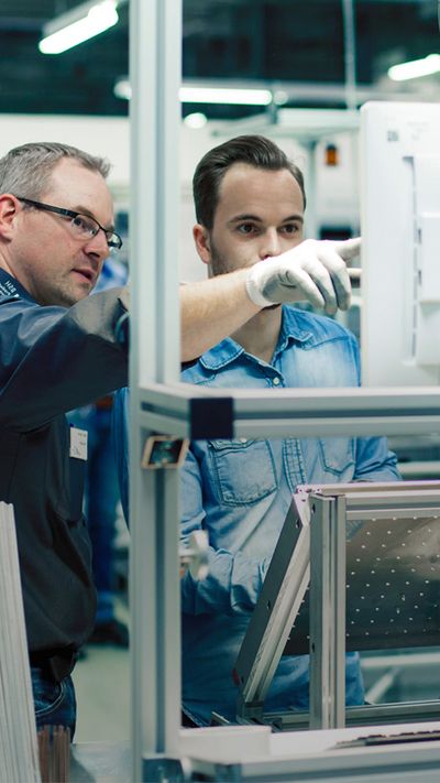 Zwei Ingenieure in einem Siemens Made in Germany Entwicklungslabor betrachten einen Monitor und zeigen darauf.