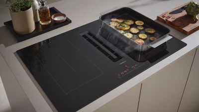Planche à induction avec plateau de cuisson, légumes et ustensiles de cuisine sur un comptoir de cuisine moderne.