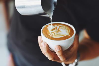 Barista nalewa parujące mleko do filiżanki latte, tworząc na powierzchni kawy misterne wzory przypominające liście i kwiaty.