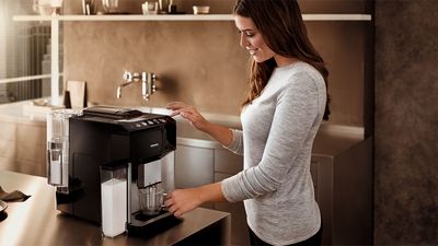 Eine Person bedient einen Siemens Kaffeevollautomaten mit Milchbehälter.
