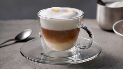 Cappuccino in einer Glastasse mit Milchschaum, Zucker und Gebäck
