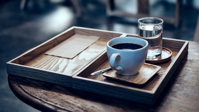 Eine Kaffeespezialiät und ein Wasser stehen auf einem Tablett auf einem Holztisch