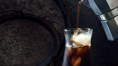 Frisch zubereiteter Iced Coffee wird ein ein Glas mit Eiswürfeln eingeschenkt