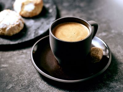 Italienischer Mokka Kaffee in einer dunklen Tasse mit Zucker und Gebäck
