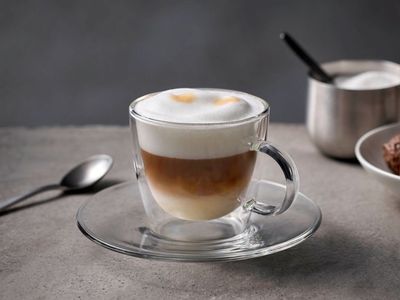 Cappuccino angerichtet mit Zucker und Gebäck in einer Glastasse