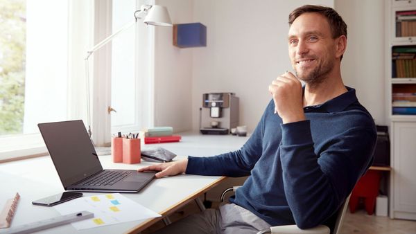 Een lachende man met een laptop aan een bureau