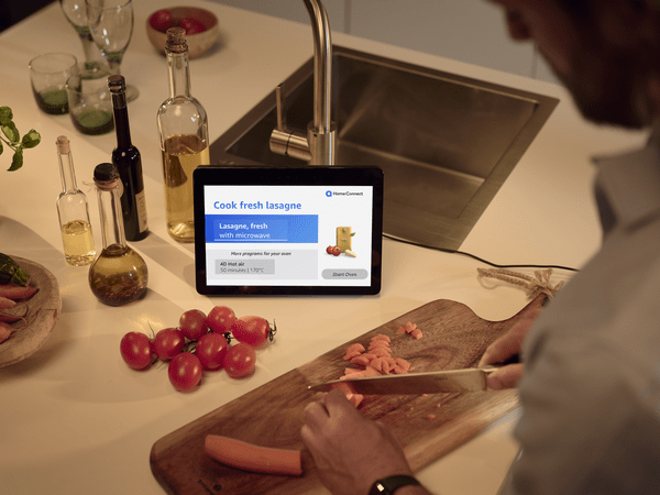 Des légumes sont coupés sur un comptoir de cuisine, lumières tamisées, Amazon Echo Show à côté de la planche à découper avec écran pour préparer des lasagnes.