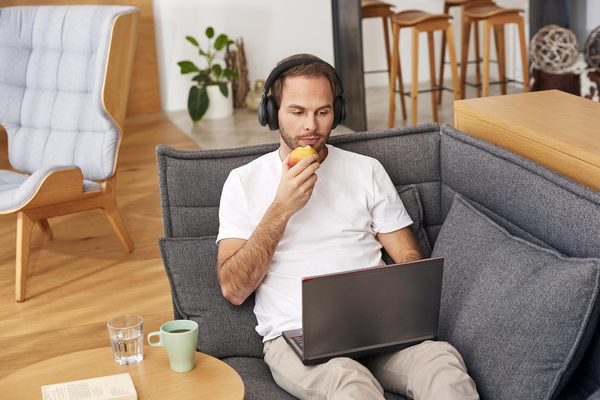 Ein Mann sitzt mit angezogenen Beinen auf seiner Couch und tippt auf seine Smartwatch, um den Roxxter unter seinen Beinen zu starten.