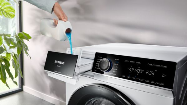 Eine Person gibt flüssiges Waschmittel in eine Siemens iQ700 Waschmaschine.