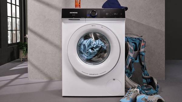 Waschmaschine Frontansicht mit dreckiger Wäsche, die daneben liegt