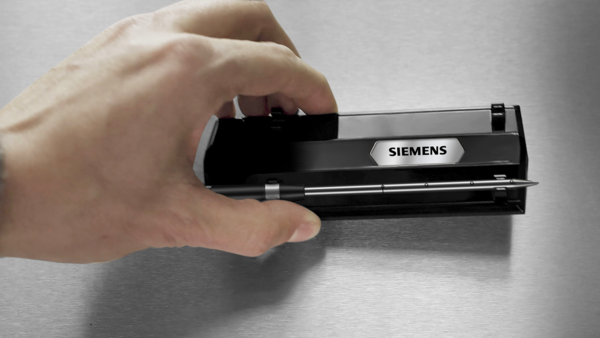 Dłoń trzymająca stację ładującą bezprzewodową termosondę marki Siemens z włożoną igłą czujnika.