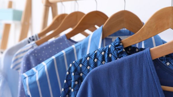 Πολλά κρεμασμένα φρεσκοπλυμένα πουκάμισα και μπλούζες σε αποχρώσεις του μπλέ.