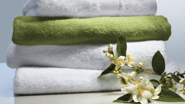 Άσπρες και πράσινες πετσέτες, διπλωμένες πάνω σε άσπρο πάγκο και μπροστά τους κομμένη μια γαρδένια.