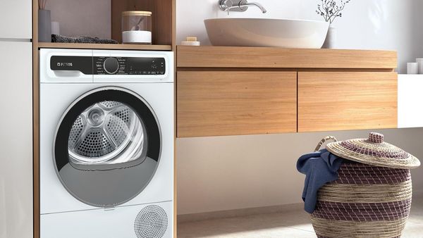 Καινούργιο μπάνιο με ένα στεγνωτήιο δίπλα από τον πάγκο του νεροχύτη, ένα ψάθινο καλάθι με άπλυτα και όλα σε γήινους και καθαρούς τόνους.