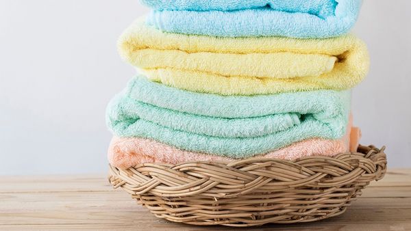 Ψάθινο καλάθι με διπλωμένες πολύχρωμες καθαρές πετσέτες μπάνιου.