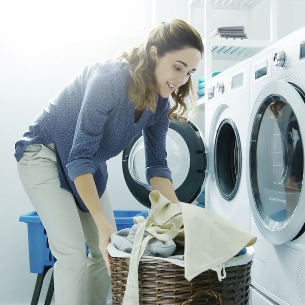 Uma mulher a sorrir enquanto coloca a roupa na máquina de lavar inteligente com a função Home Connect