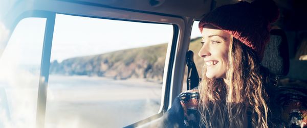 Home Connect: Lachende junge Frau schaut aus dem Fenster eines Autos