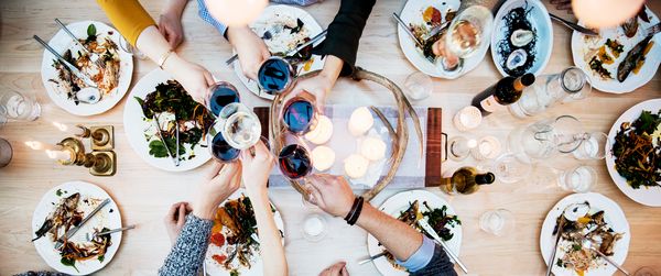 Freunde sitzen am Esstisch und stoßen gemeinsam mit einem Glas Wein an. Kein Problem, dank Home Connect.