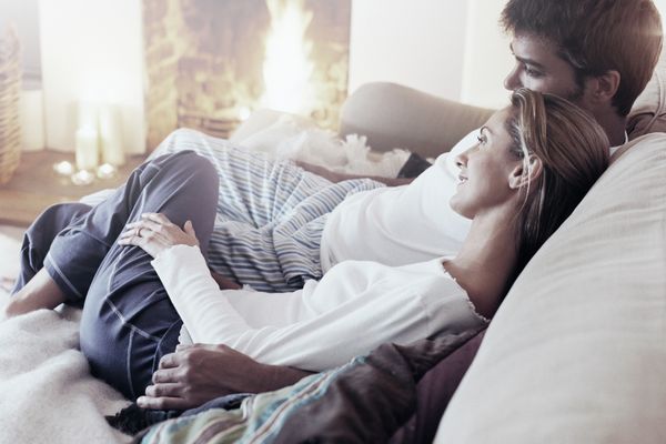 Un couple sourit sur le canapé du salon, devant un feu de cheminée.