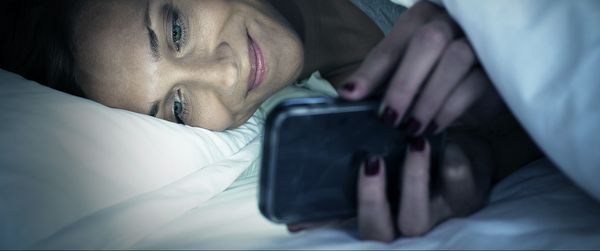 Frau liegt mit ihrem Smartphone im Bett