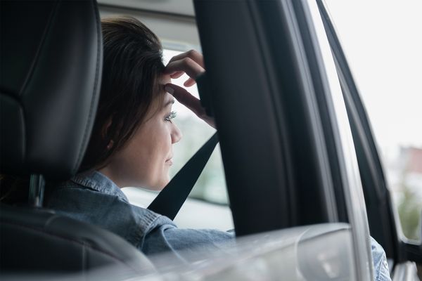 Uma jovem mulher num carro a monitorizar os eletrodomésticos Home Connect enquanto está fora