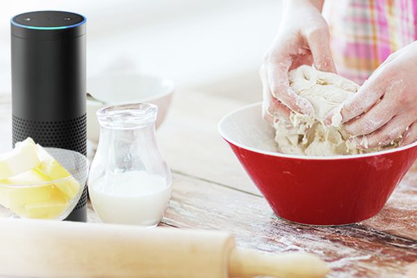 Amazon Echo steht auf einer Arbeitsfläche auf der gerade ein Teig zum Backen in einem Ofen mit Home Connect Funktion geknetet wird