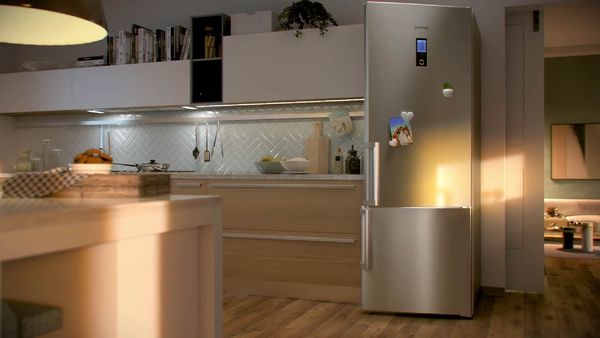 Μια μοντερνα κουζίνα με ξύλινους πάγκους, με ψυγειοκταψύκτη pitsos σε ασημί χρώμα, όπου φωτίζει την κουζίνα οι ακτίνες του ήλιου.