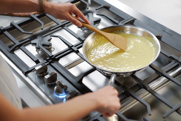 Thermador gas cooktop with woman stiring sauce in pan 
