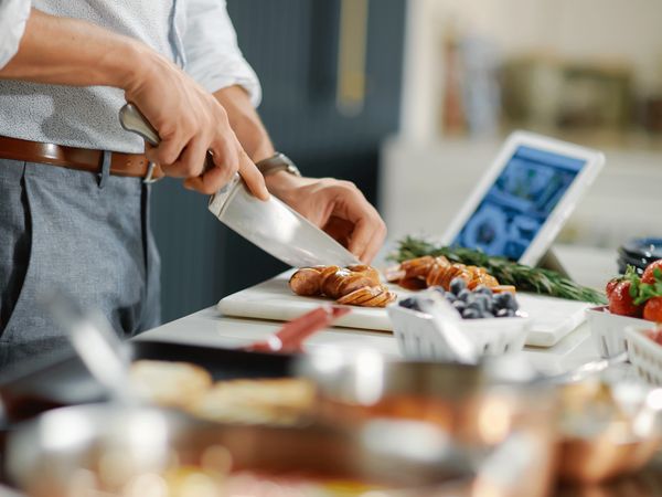 Thermador Connected Experience shown on tablet screen next to man cutting food in the kitchen