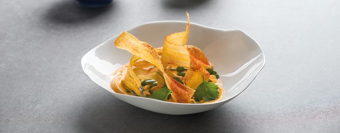 Un piatto gourmet con una salsa cremosa, condita con erbe verdi vivaci e nastri di verdure dorate e croccanti in una ciotola bianca.