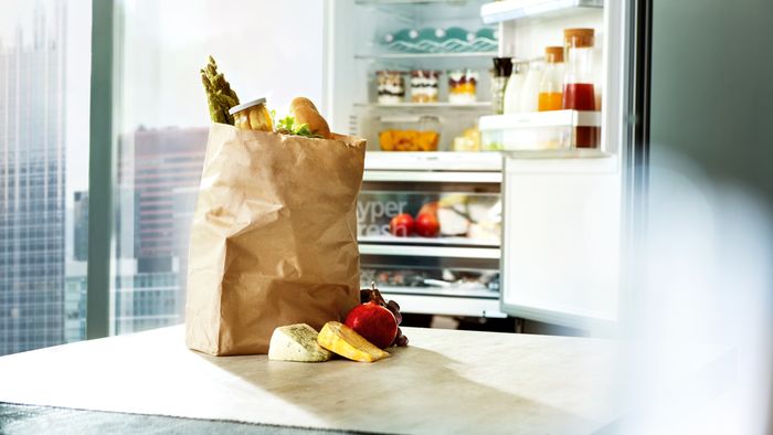 Brown bag of food products on worktop infront of open fridge showing inside contents
