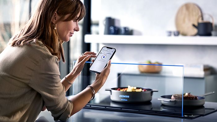 Donna che comanda i suoi elettrodomestici intelligenti della cucina dall’App dello smartphone