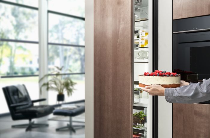 Persona che inserisce una torta con frutti di bosco nel frigorifero smart Siemens