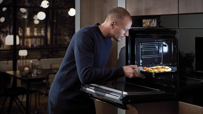 Ragazzo con teglia di pizza nel forno Siemens iQ700 dotato di telecamera interna e intelligenza artificiale