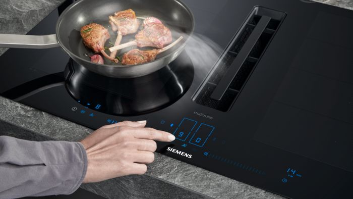 Padella con carne sul piano inductionAir Plus di Siemens, con mano femminile che regola l’intensità di cottura