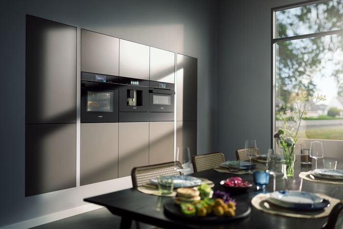 Visuale di una cucina moderna con parete con dispensa ed elettrodomestici e tavolo in primo piano
