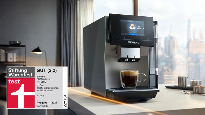 Ein Siemens Kaffeevollautomat EQ700 mit einer gefüllten Tasse Kaffee. Daneben ist das Testsiegel der Stiftung Warentest zu sehen.